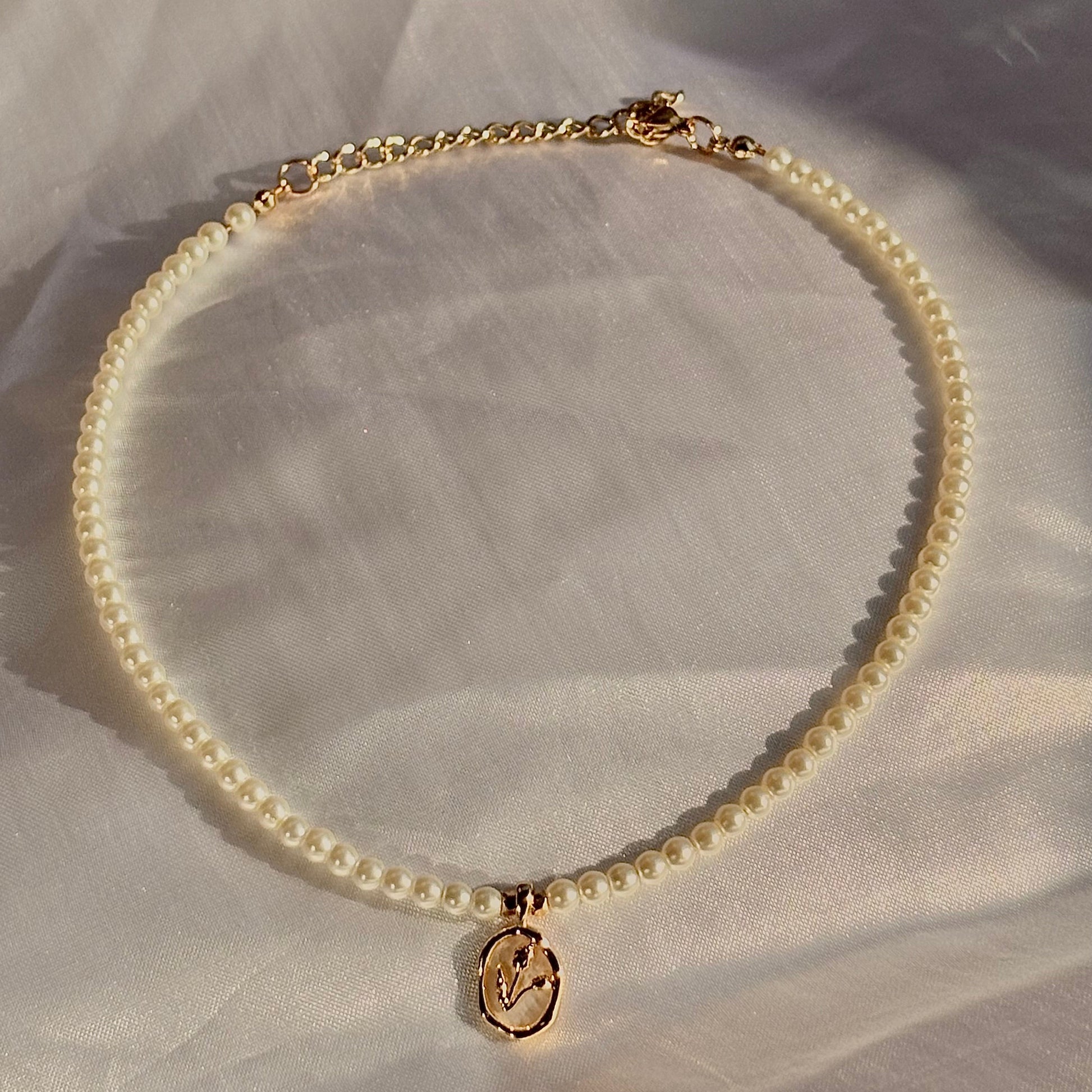 Pearl necklace with a gold charm on a light fabric background