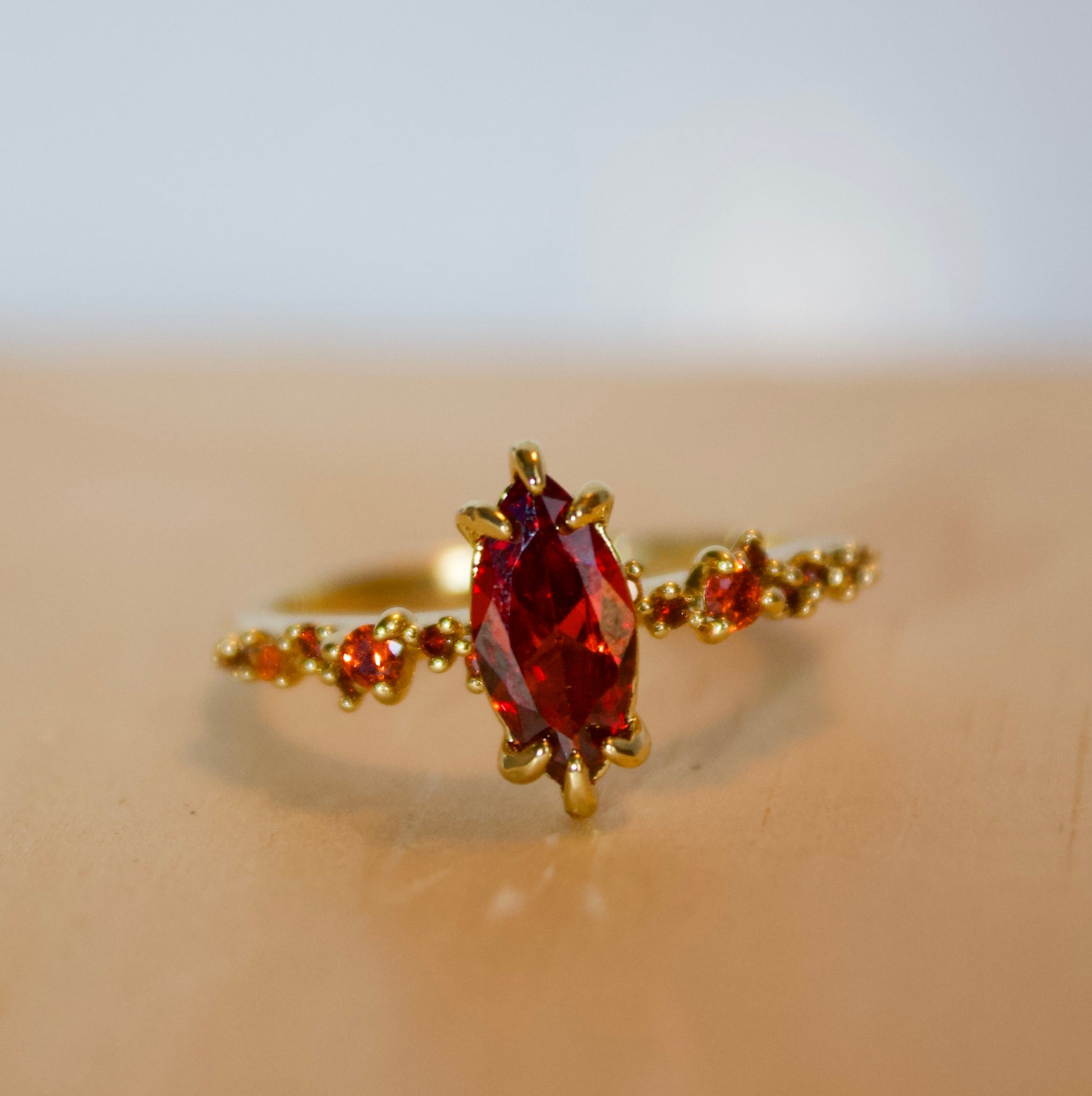 Gold ring with a red gemstone on a beige surface