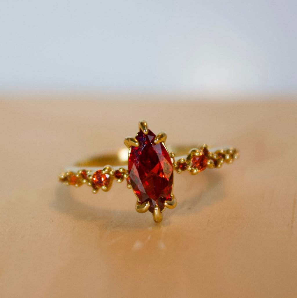 Gold ring with a red gemstone on a beige surface