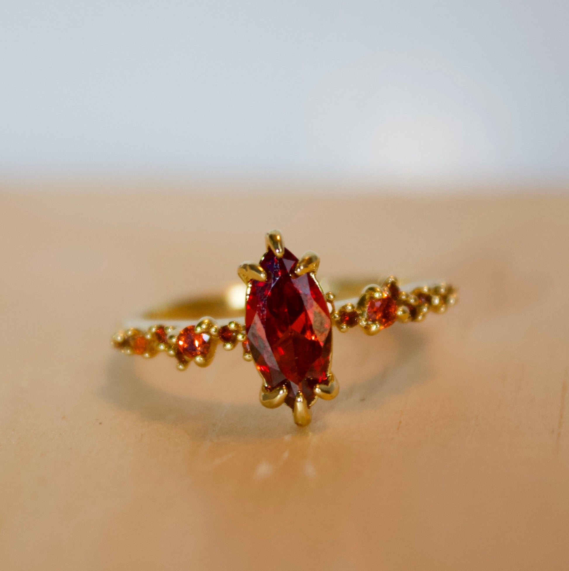 Gold ring with a red gemstone on a beige surface
